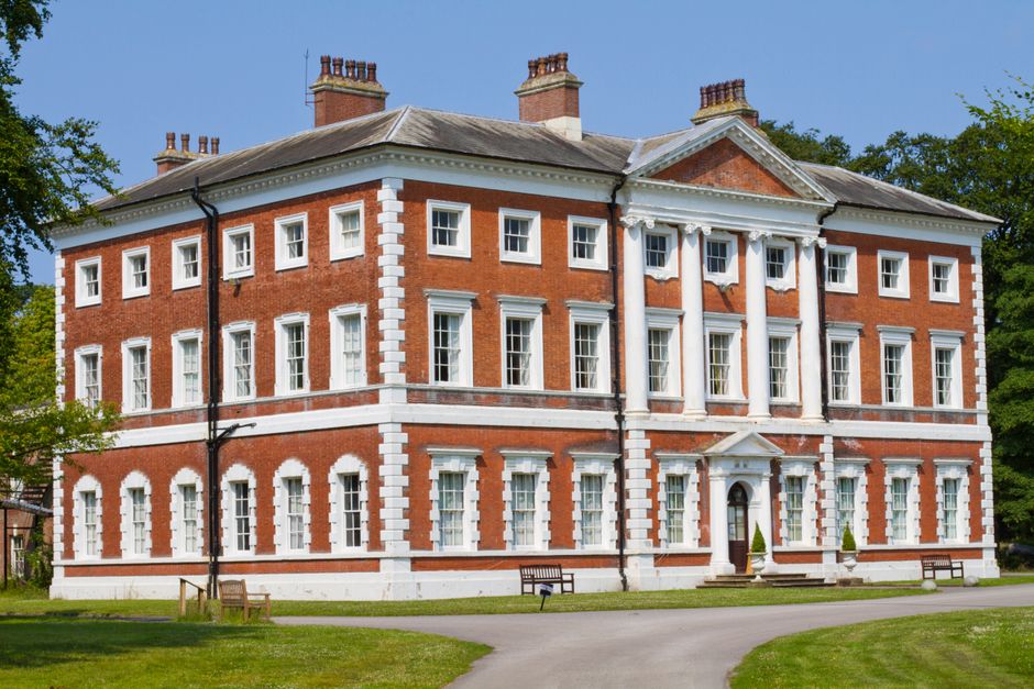 A large historic brick building with medieval castle-like features, including crenellated battlements along the roofline and a prominent tower with narrow windows. The facade shows multiple large, whi